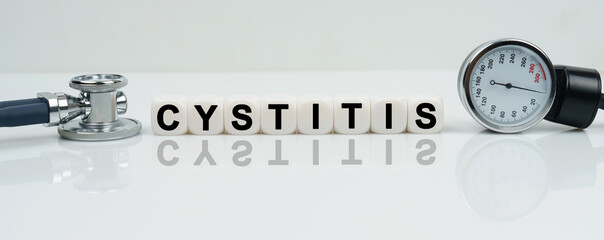 On a reflective white surface lies a stethoscope and cubes with the inscription - CYSTITIS