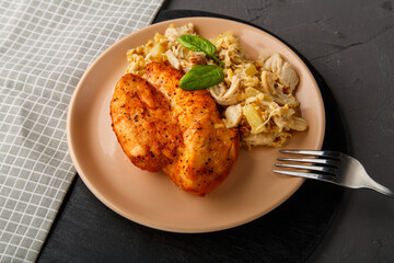Baked chicken breast with salad on a plate decorated with spinach next to a fork on a concrete background on a gray napkin.
