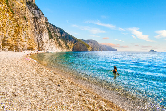 A woman wades in the turquoise blue green sea off of the secluded Paradise, or Chomi Beach on the island of Corfu, Greece.