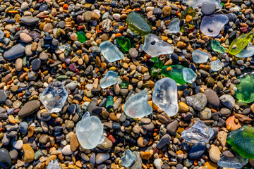 Some pieces of glass moulded by the sea on the pebble beach. The texture of colored stone beach