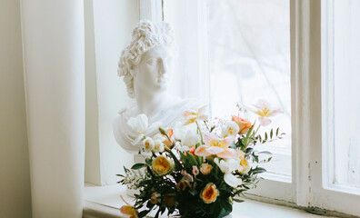 A statue of a bust of a woman stands on the window next to a bouquet of flowers, a concept of spring and International Women's Day