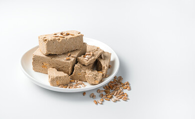 A white plate with halva is sprinkled with sunflower seeds on a light background.