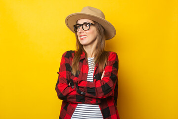 Young woman with a smile in a hat and a plaid shirt looks to the side on a yellow background