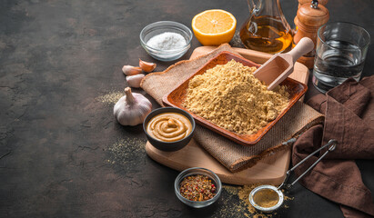 Mustard powder, ready-made mustard, spices, lemon, garlic and oil on a brown background.
