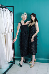 Beautiful girls in black dresses, against the background of a beautiful wall. The blonde put her hand on the brunette's shoulder.