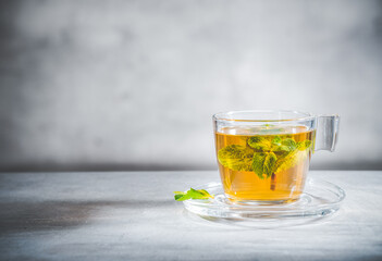 Mint tea with leaves in glass cup on gray background, front view