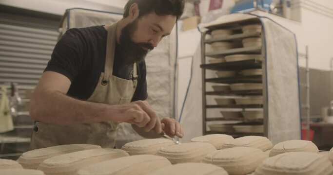 Baker cutting with knife decoration in sourdough dough before baking in oven