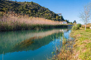 River crossing a marsh with reeds, and some mountains in the background, with a blue and clean sky. In Oliva (Valencia, Spain).
