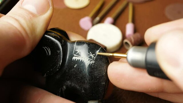 A professional jeweler engraves on a stone figurine to create a piece of jewelry.