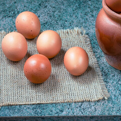 a few fresh chicken eggs on a cloth napkin and in a ceramic bowl on a wooden background. Healthy eating concept