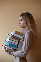 Charming woman with curly hair carries a stack of books on a beige background