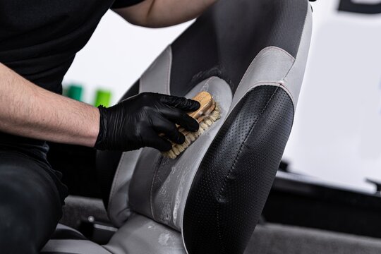 Man car wash worker cleaning leather boat seat with brush and detergent