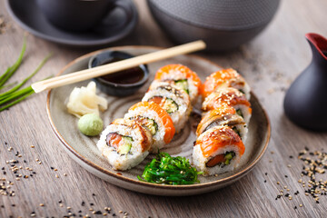 Sushi maki rolls with salmon, eel, avocado, cucumber on a plate with chopsticks, soy sauce, wasabi and ginger. Japanese traditional fish food closeup served for lunch in modern gourmet restaurant