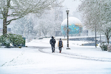 Duringa snow storm, two men walking in riverfront park with the eco-earth globe map in background,...