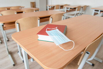 Book with a disposable protective mask on school table. Back to school  after pandemic