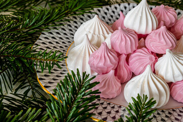 Obraz na płótnie Canvas White and pink meringues on a porcelain plate surrounded by green pine branches.