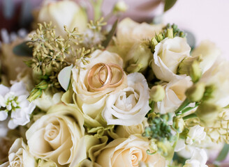 Close up view of two gold wedding rings lying on the roses bouquet.