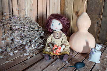 A textile interior doll sits on a wooden background with a pumpkin, dried flowers and a mouse.