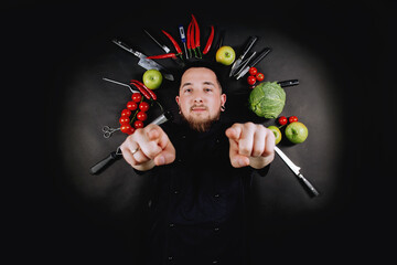 Chef flat lay composition. Top view. Chef cook lies between vegetables on a black background. Culinary background with fresh raw vegetables and kitchen tools on a black background.