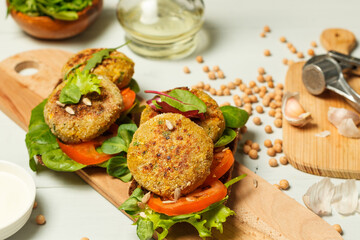 Two sandwiches with chickpea cutlets and green salad, on a wooden tray. Chickpeas and garlic in the background.Close-up, selective focus
