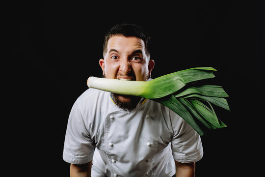 Leek in the mouth of the chef. The chef holds a leek. Man with leeks in his mouth.