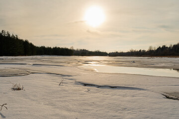 Misty calm evening on the forest lake is illuminated by the colors of sunset, melting ice, reflection in the water mirror.
