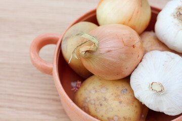 A lot of vegetables. Red onions. garlic and potato in a yellow pot. Wooden table background