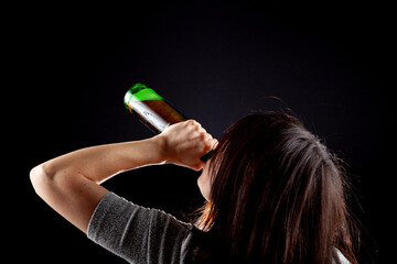 Rim light from behind image of a young caucasian woman drinking beer from bottle against dark background. She has long brown hair and short sleeve t shirt. Versatile Alcohol related concept image.