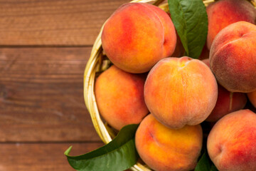 Fresh juicy peaches with leaves in a wicker basket on a wooden background. Freshlypicked peaches in a wicker basket