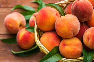 Fresh juicy peaches with leaves in a wicker basket on a wooden background. Freshlypicked peaches in a wicker basket