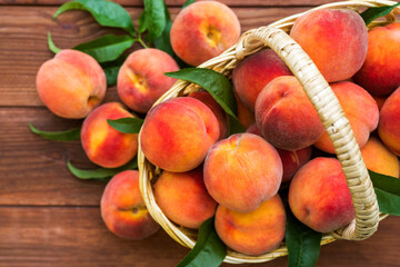 Fresh juicy peaches with leaves in a wicker basket on a wooden background. Freshlypicked peaches in a wicker basket