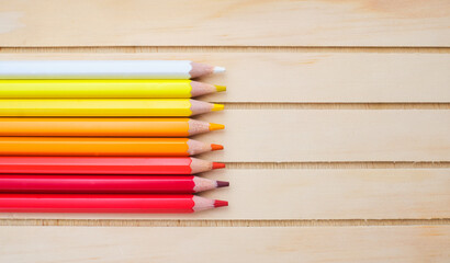 Fototapeta premium Composition with white, yellow, orange, red pencils on wood background, top view