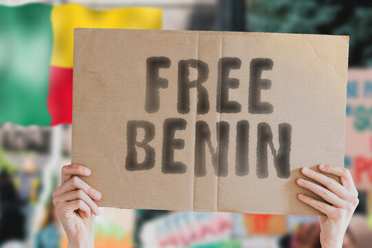 The phrase " Free Benin " on a banner in men's hand with blurred Beninese flag on the background. Protest. Riot. Violence. Economic crisis. Collapse. Politics. Streets. Save. Cruelty