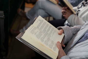 Eine Frau sitzt in der Kirche und singt nach dem Kirchenblatt mit. Das Kirchenblatt, Notenbuch ist...