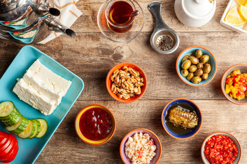 Healthy Turkish breakfast, with sliced tomato, cucumber, and white feta cheese, small bowls of strawberry jam, olive, honey, pepper paste. Tea is served in traditional Turkish tea glass. Ramadan feast