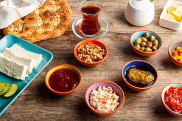 Healthy Turkish breakfast, with sliced tomato, cucumber, and white feta cheese, small bowls of strawberry jam, olive, honey, pepper paste. Tea is served in traditional Turkish tea glass. Ramadan feast