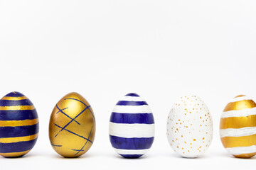 Five easter eggs trendy colored classic blue, white and golden decorated on white table. Happy Easter card with copy space for text. Minimal style.
