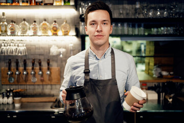 A male barista bar employee makes a takeaway coffee. Works in his small business restaurant cafe. Copy space.