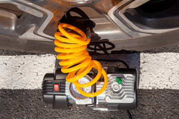 Close up top view image of a small 12 v air compressor attached to the stem valve of a car tire to...