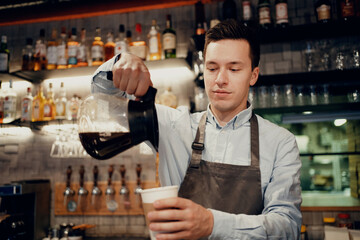 A male barista bar employee makes a takeaway coffee. Works in his small business restaurant cafe. Copy space. Modern interior.