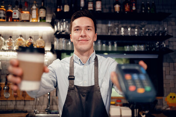 Payment via the bank's NFS terminal from a mobile phone. A satisfied barista brews and sells coffee to take away. Paper cup with a drink Americano, espresso, cappuccino.