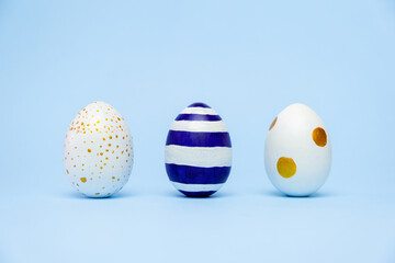 Three easter trendy colored classic blue and golden decorated eggs striped pattern on blue. Happy Easter card with copy space for text. Minimal style.