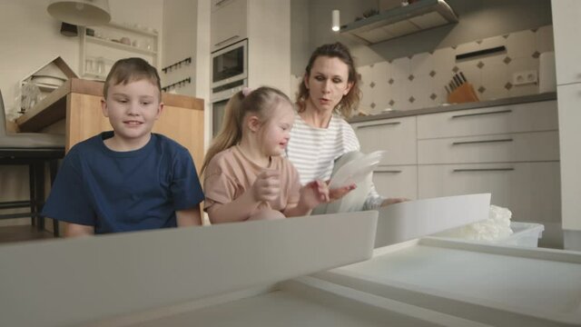 Lockdown of beautiful middle-aged Caucasian woman teaching her son and little daughter with down syndrome how to segregate rubbish at home