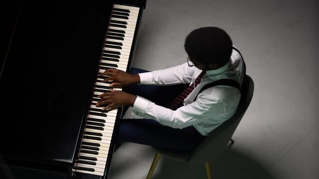 Top view of stylish man playing grand piano. The African American touches the black and white keys with his fingers to create the rhythm of the melody. Close up of a black male pianist.