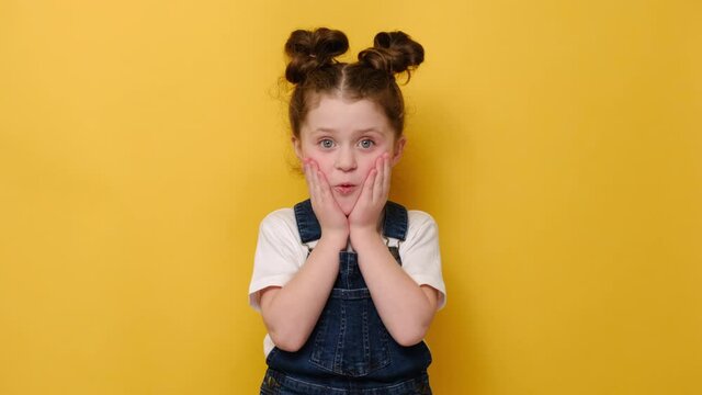 Portrait of surprised little preschool girl look at camera feel stunned amazed by unexpected good news, happy cute small child shocked by unbelievable surprise, isolated on yellow studio background