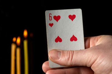 Card six in the hand of a fortune teller close-up on a black background and burning candles. It іs a long haul prediction