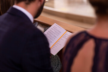 Ein Mann  sitzt in der Kirche und singt nach dem Kirchenblatt mit. Das Kirchenblatt, Notenbuch ist...