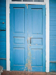 Obraz na płótnie Canvas The rickety and curve shabby wooden door to the house. The door is painted with blue paint, the door frame is painted with white paint.