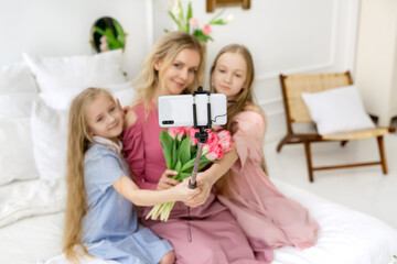 Two daughters and a mother take selfies on their phone. The girls gave their mother a bouquet of tulips and are photographed as a souvenir. Cute and beautiful girls.