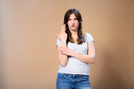 young girl with pigtails imitates a gun with her hand on a beige background.